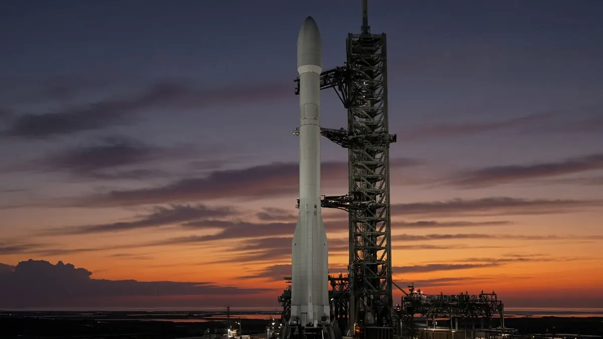 Rocket launch gantry silhouetted against a purple and orange dusk sky