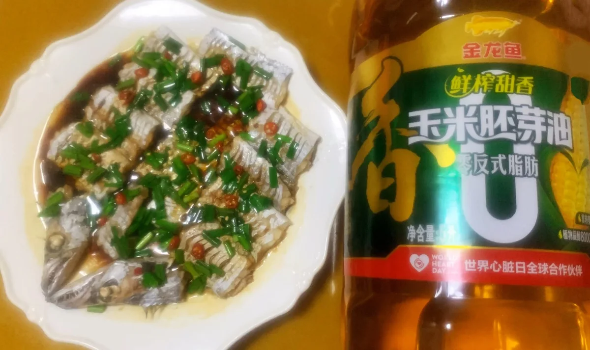 Steamed beltfish segments under chopped chili and scallion in a soy glaze, beside a bottle of corn germ oil