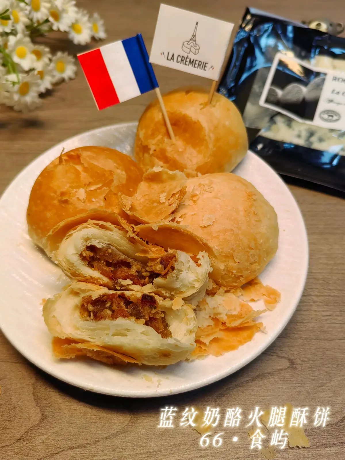 Flaky round pastries on a white plate, one broken open to show the ham filling, a package of blue cheese behind