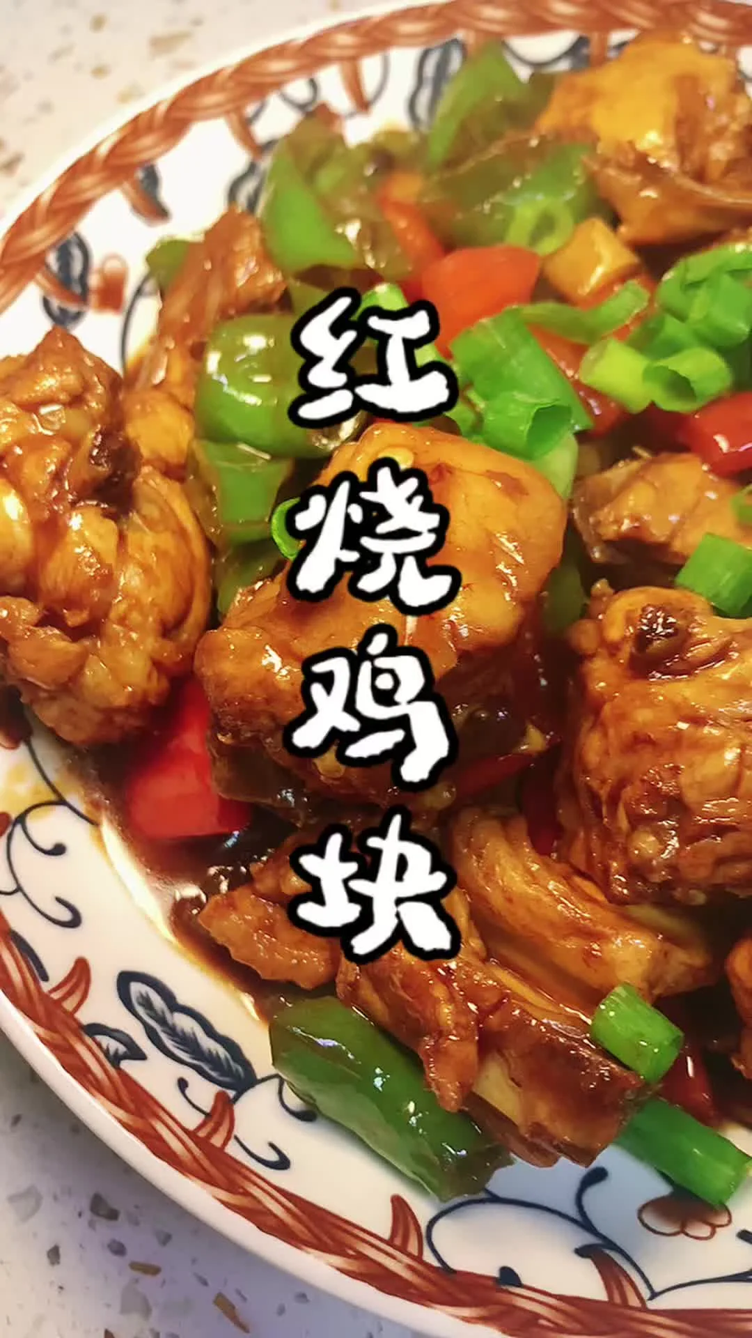 A close-up of glossy red-braised chicken pieces with green and red peppers on a patterned plate