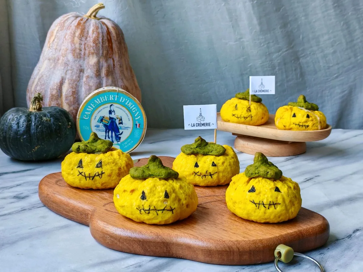 Pumpkin-shaped yellow scones with chocolate jack-o-lantern faces and matcha stems on a wooden board