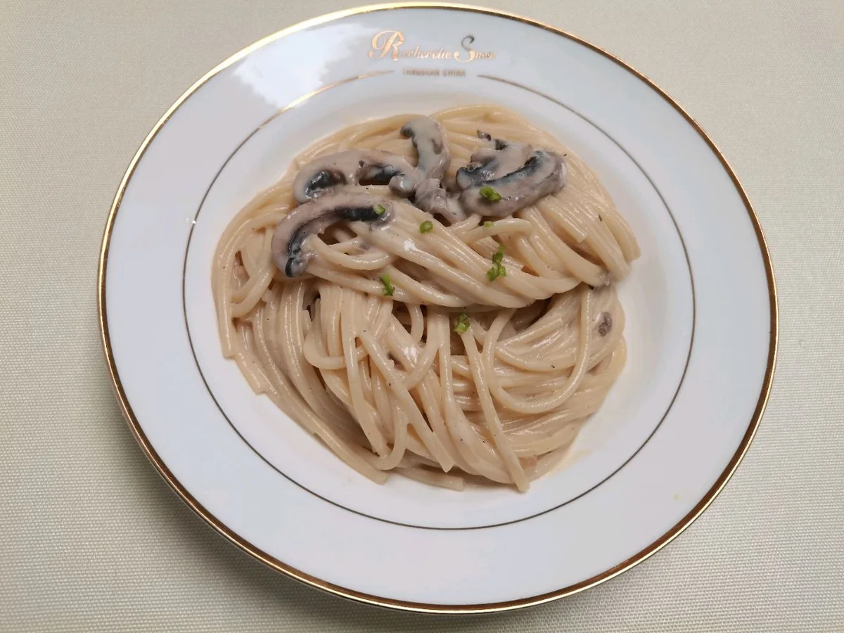 A plate of creamy spaghetti topped with sliced mushrooms and chopped scallion