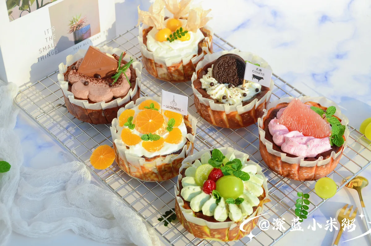 Six small Basque cheesecakes in different colours topped with piped cream and fruit