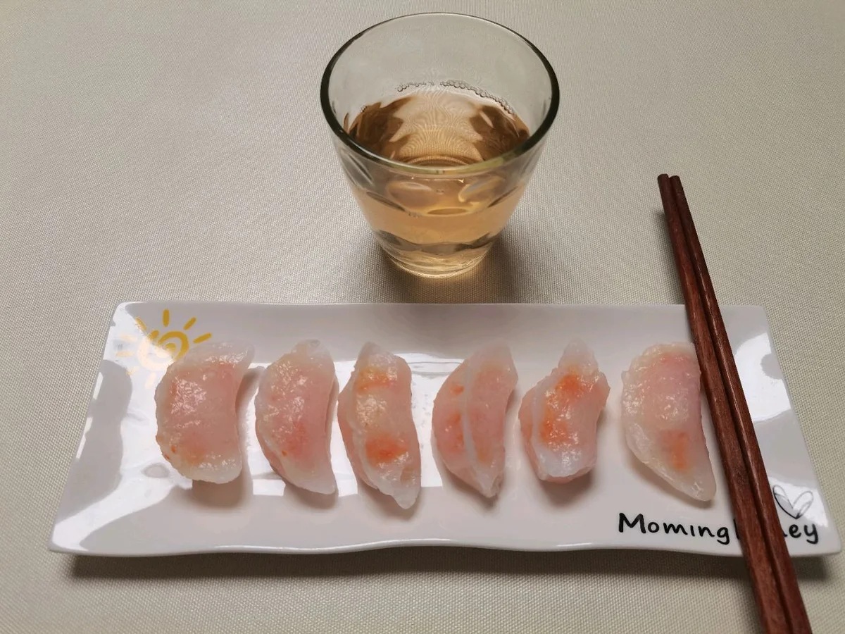 Translucent shrimp dumplings lined up on a white plate beside a glass of tea