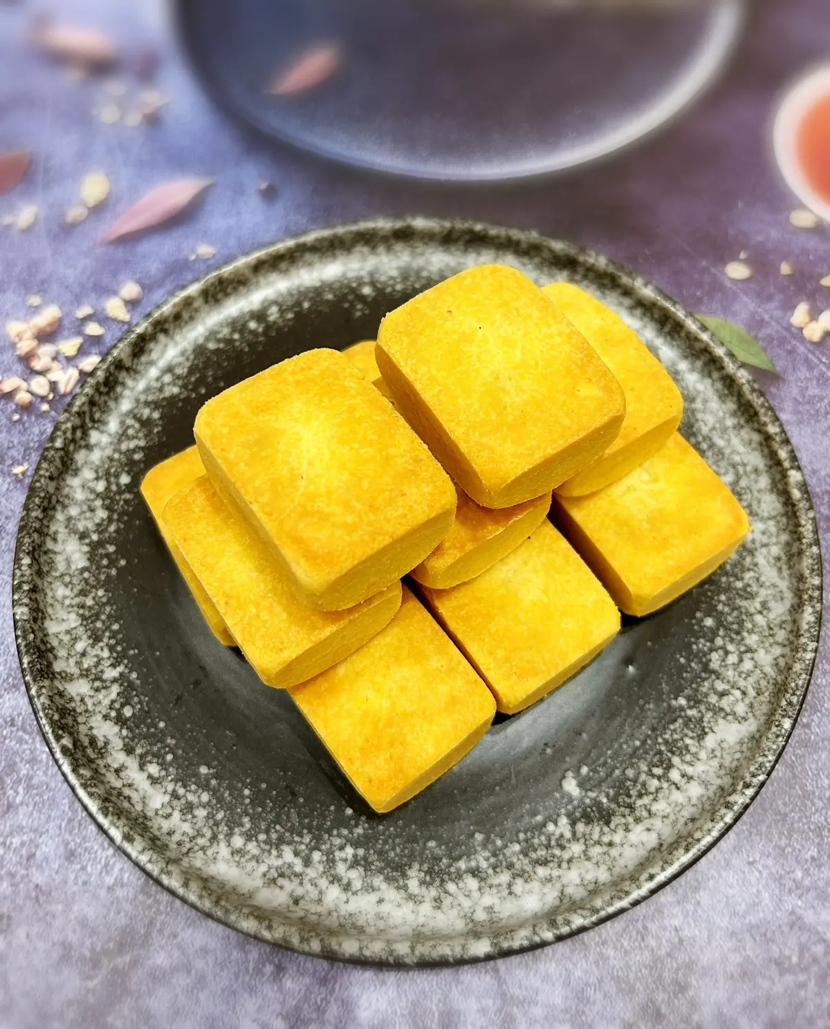 Square golden pineapple cakes stacked on a dark ceramic plate