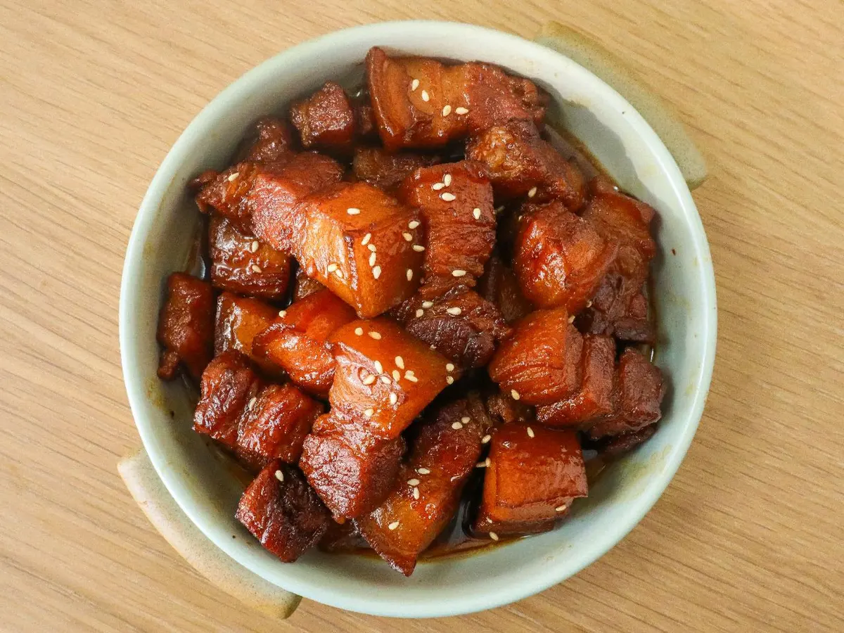Glossy cubes of red-braised pork belly scattered with sesame in a light bowl