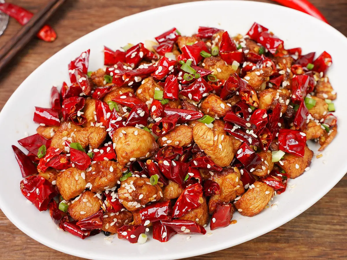 Fried chicken pieces tossed with dried red chillies and sesame on a white plate