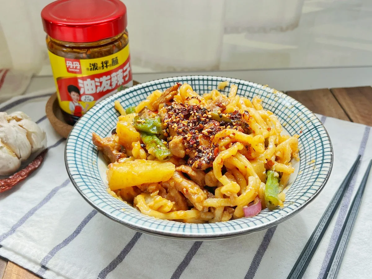 A bowl of braised noodles with green beans and potato strands on top