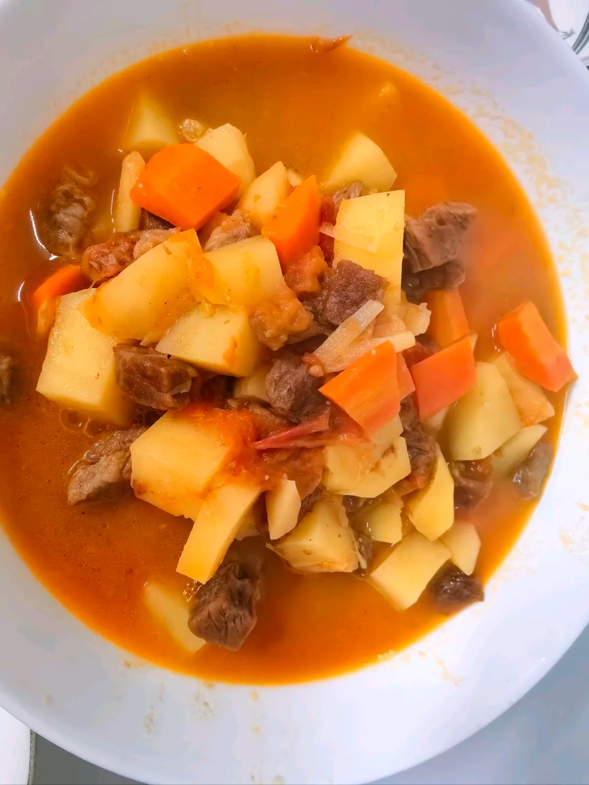 Beef, potato and carrot chunks in a tomato-red broth in a white bowl