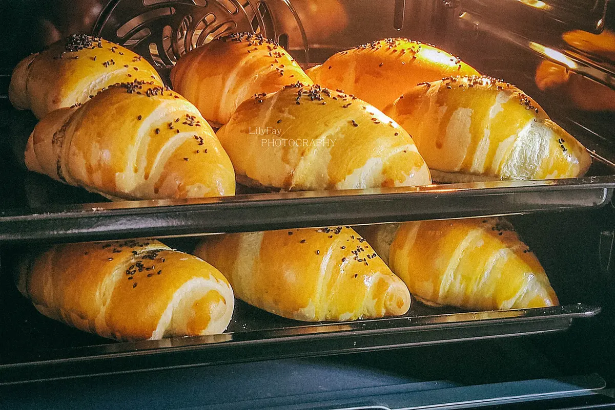 Golden bread rolls with split tops baking on two trays in an oven