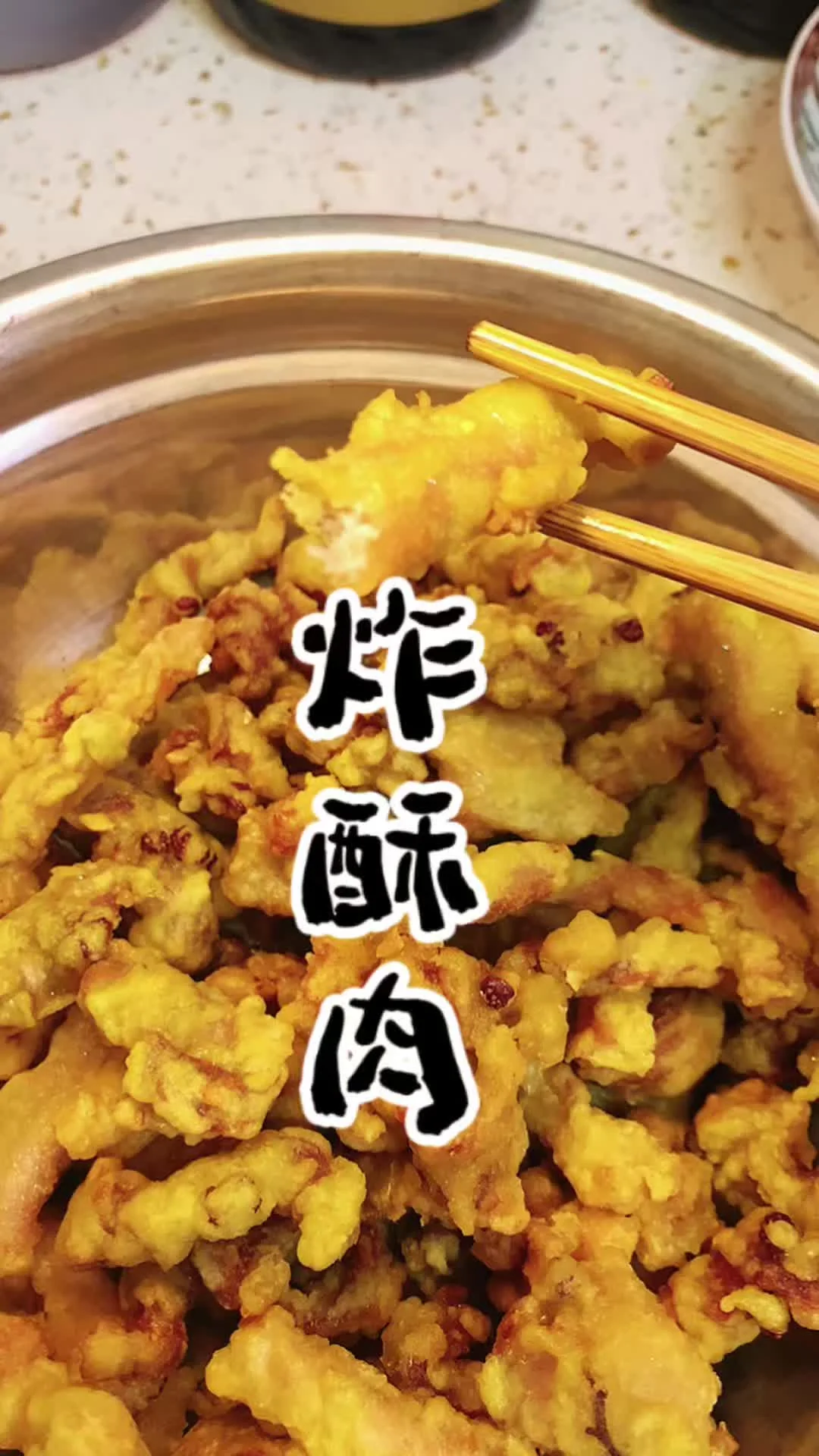 Golden batter coated pork strips piled in a steel bowl with chopsticks lifting one