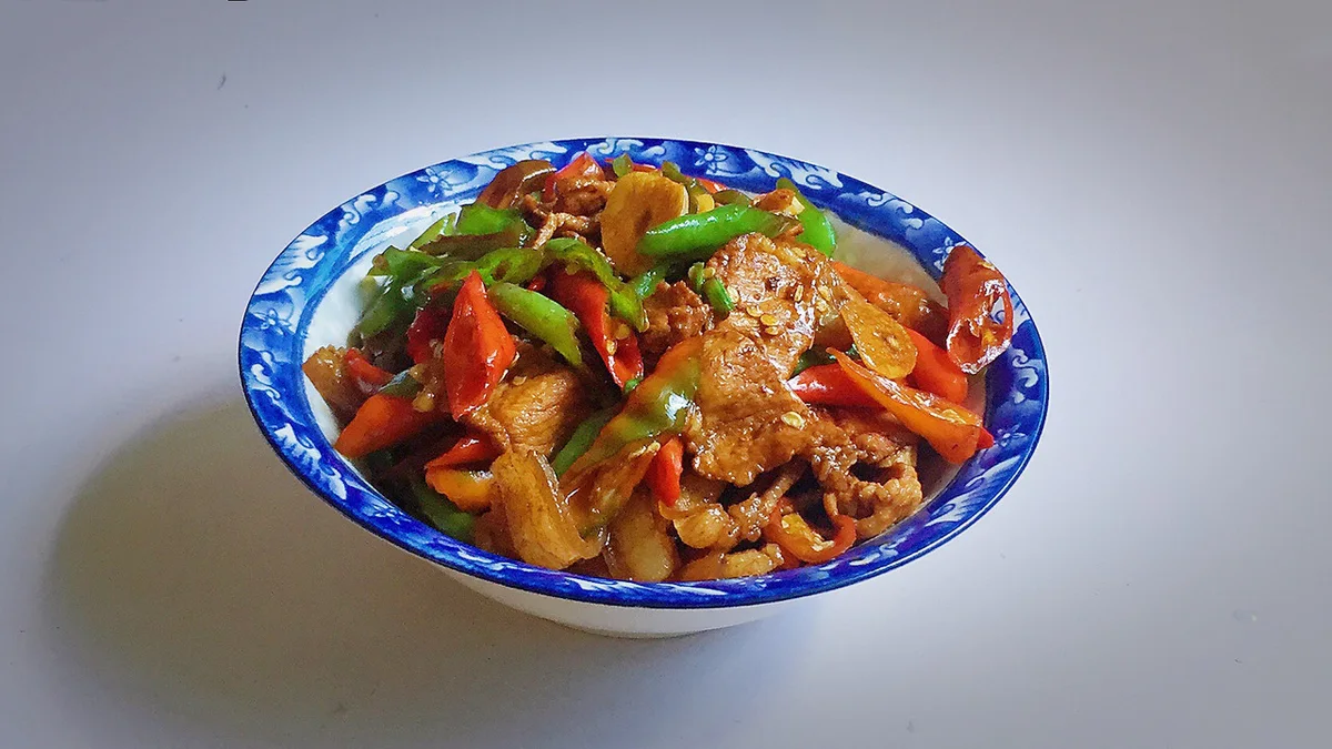 A blue and white bowl of stir fried pork slices with red and green chillies