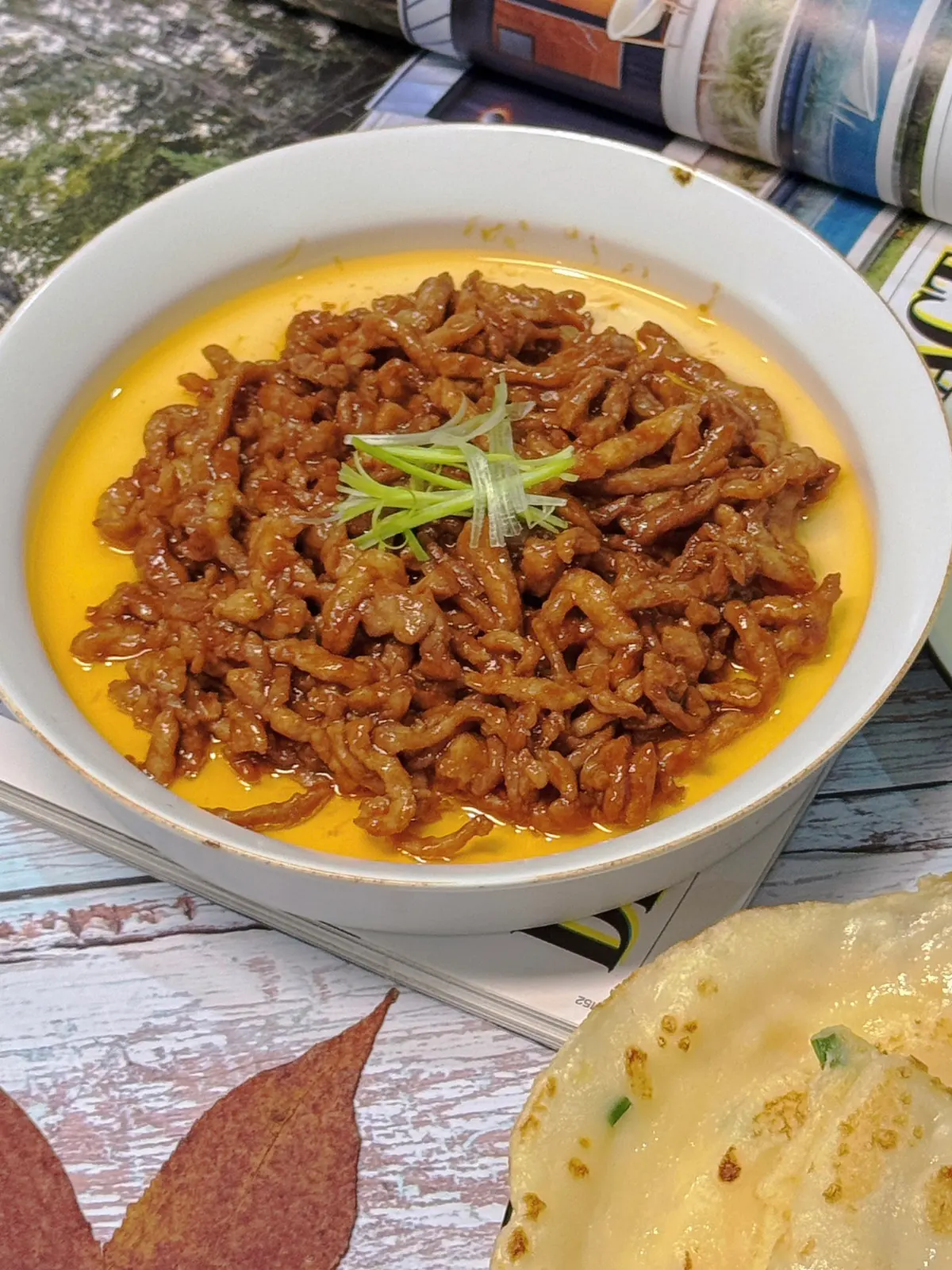 Glossy shredded pork in dark sweet bean sauce in a white bowl topped with scallion shreds