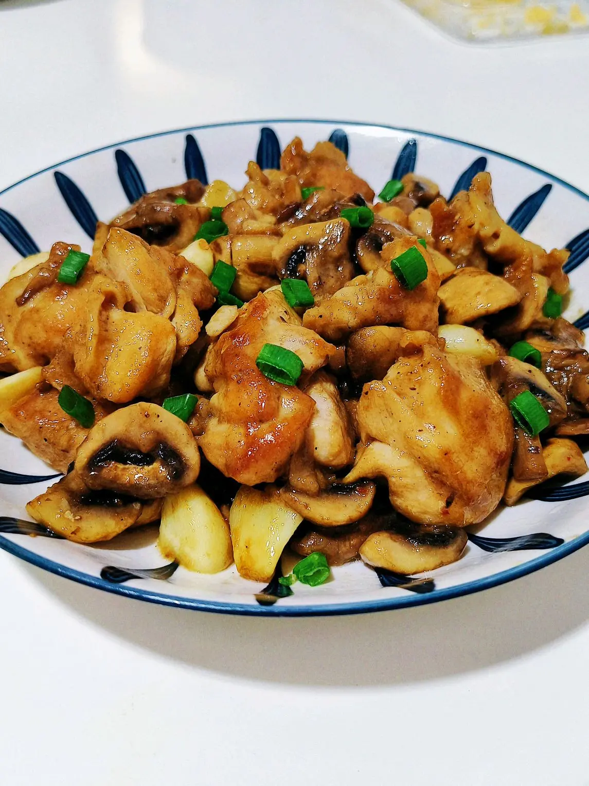 Golden seared chicken thigh chunks tossed with browned button mushroom quarters and soft garlic cloves in a black pan