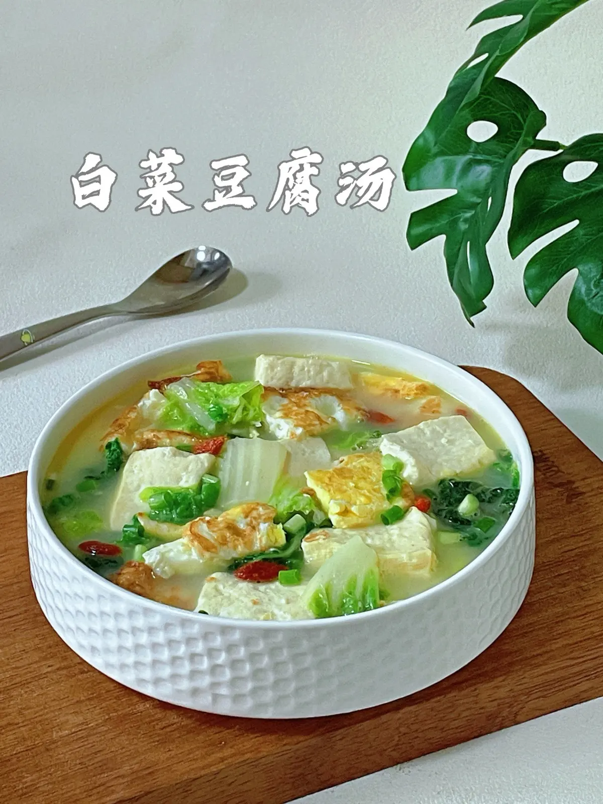 A white bowl of milky soup with tofu cubes cabbage leaves and golden fried egg chunks