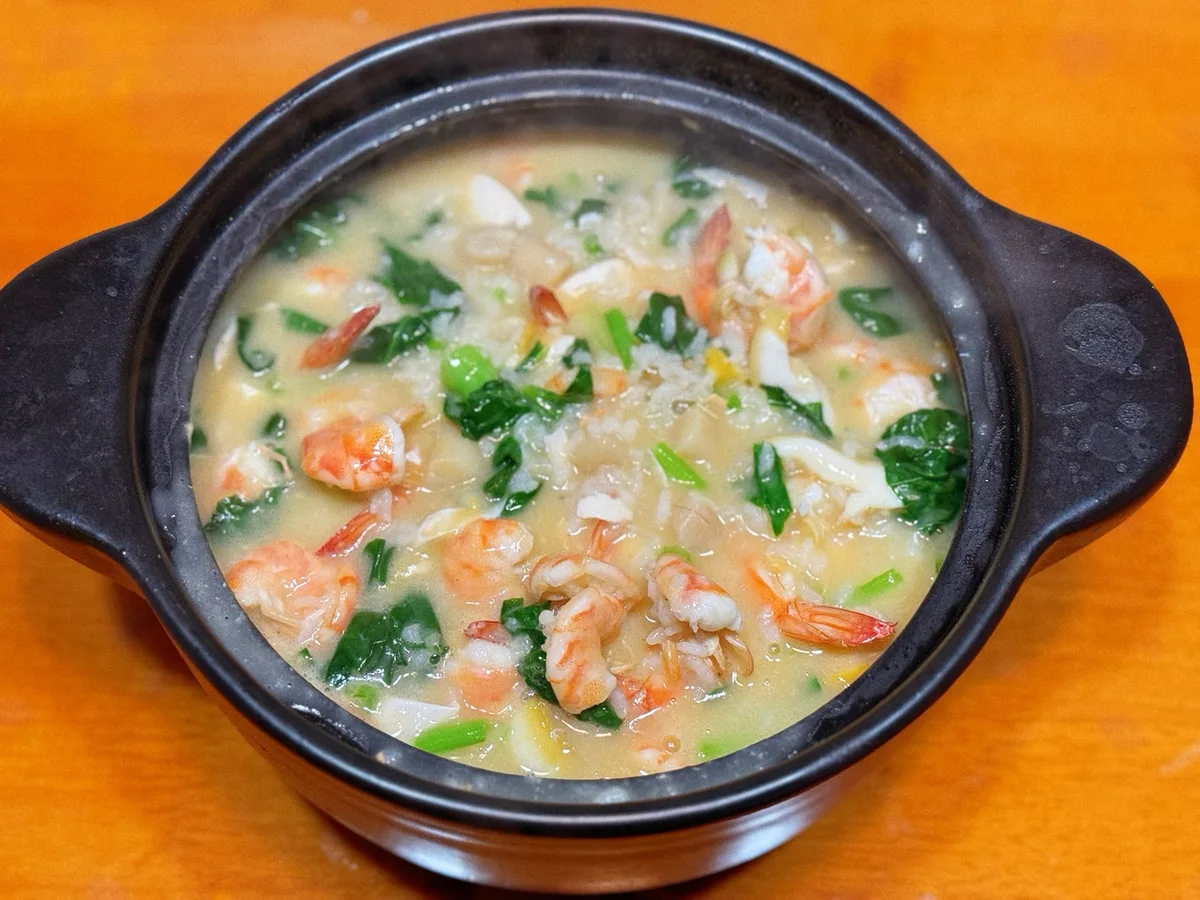 A claypot of thick seafood congee with whole prawns abalone slices and green vegetables