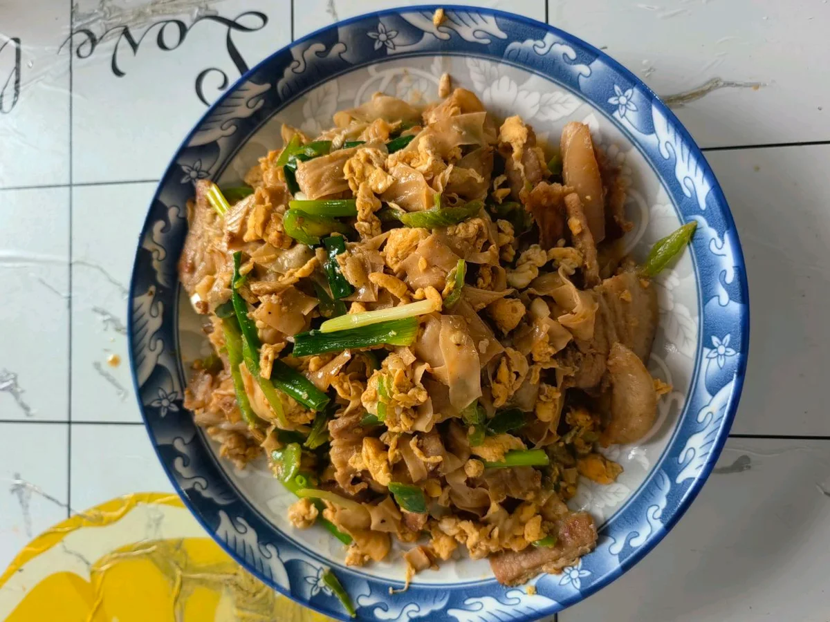 A blue-rimmed plate of sliced pork belly with softened soy protein sheets, scrambled egg and scallion sections