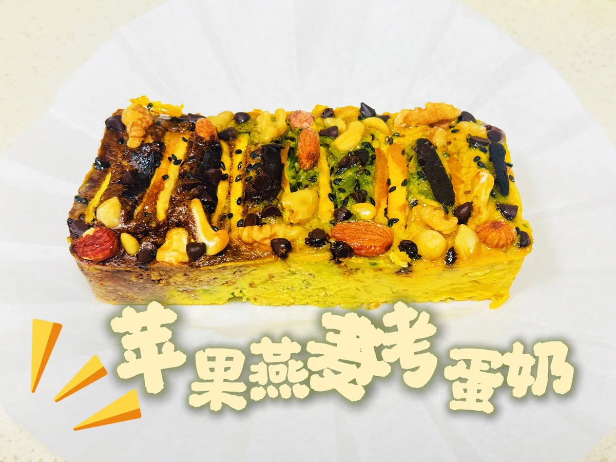 A rectangular slab of baked apple oat custard topped with mixed nuts, chocolate chips and black sesame on parchment paper