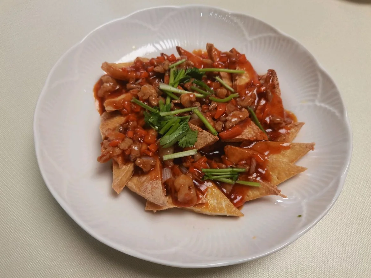 A plate of golden pan-fried tofu triangles topped with a reddish minced pork and tomato sauce and cilantro