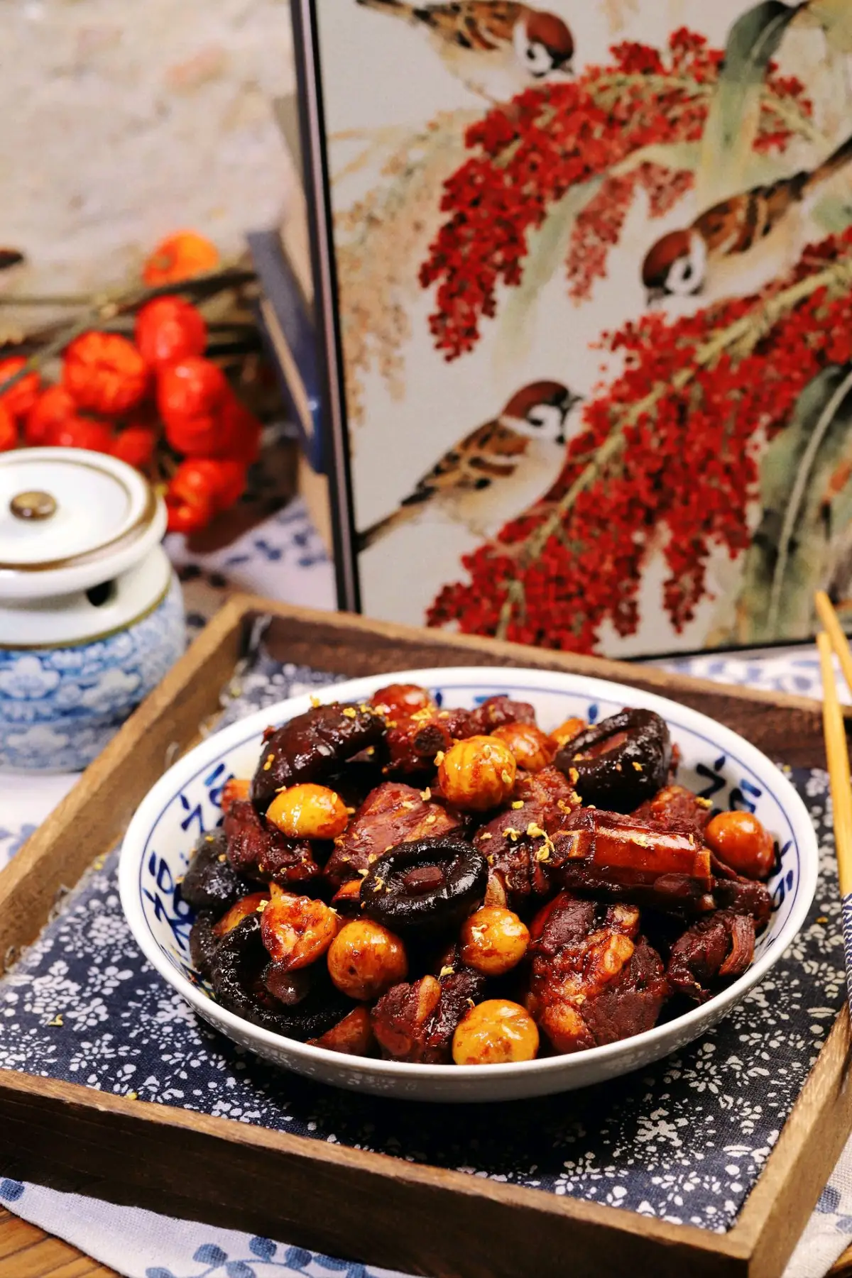 A blue and white bowl of braised pork ribs with whole chestnuts and dark shiitake in a glossy mahogany sauce on a wooden tray