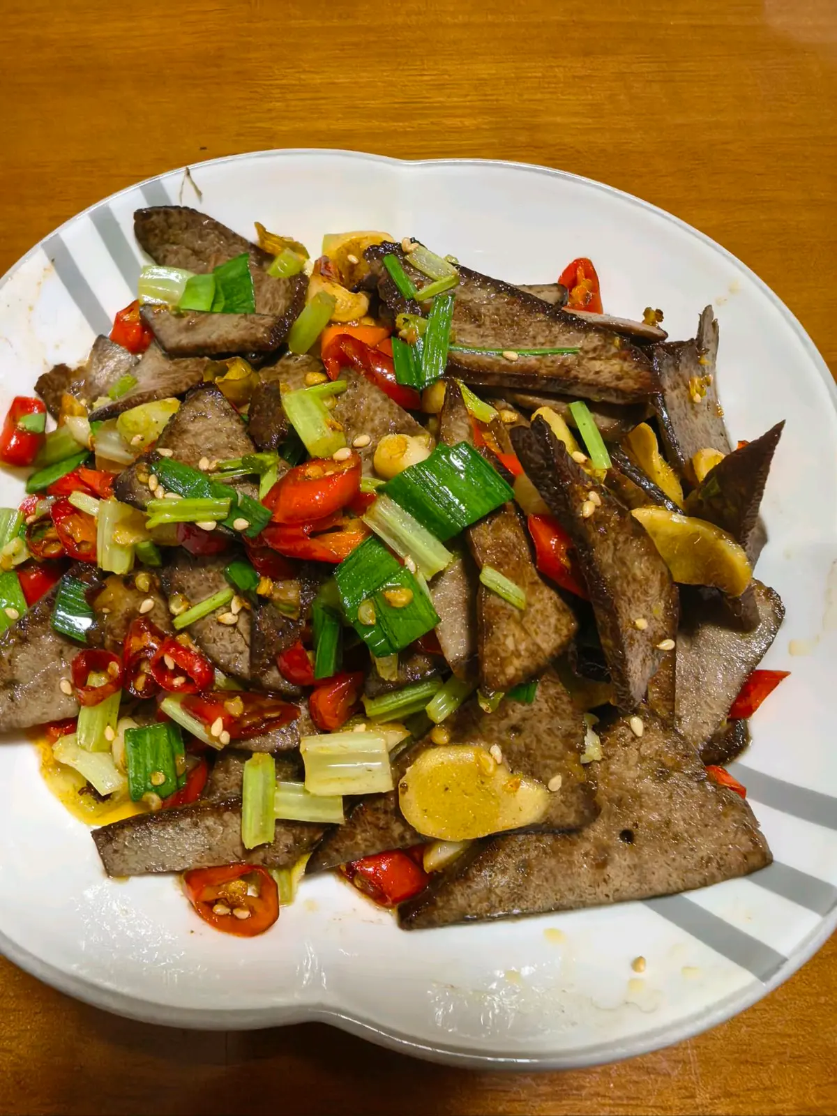 Thin sliced braised pork liver tossed with red bird's-eye chilies, celery, garlic sprout leaves and toasted sesame on a white plate