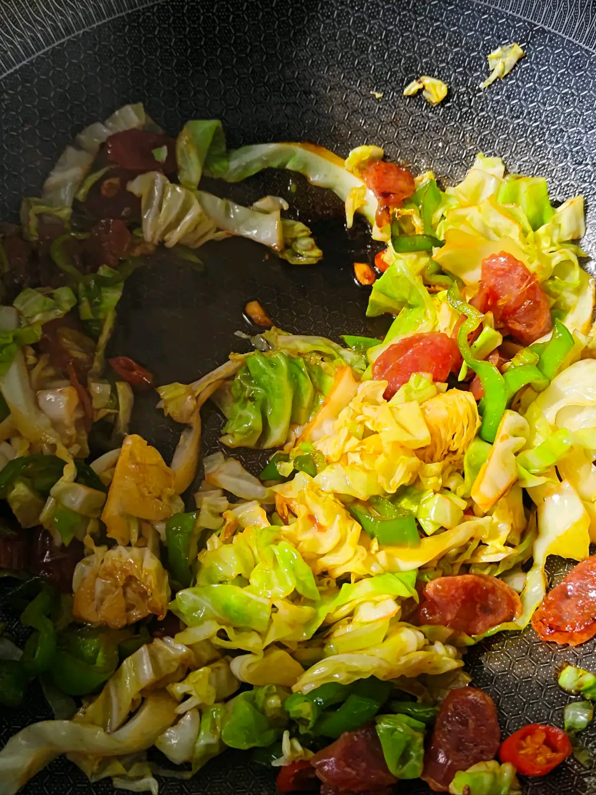 Sliced Chinese sausage and shredded cabbage tossed with green pepper pieces in a wok