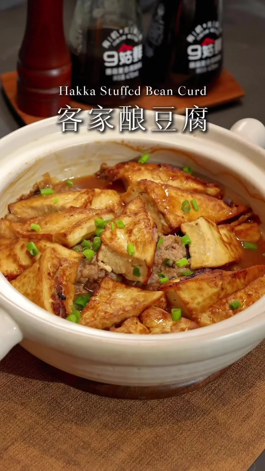 Pan-fried tofu triangles stuffed with pork in a white claypot, glossy brown sauce and chopped scallions on top