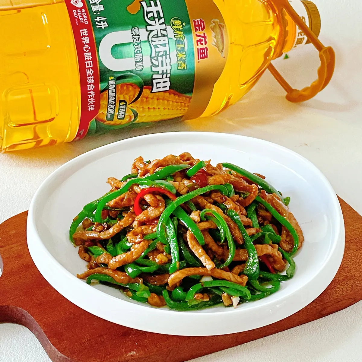 Shredded pork and green pepper strips piled in a white bowl on a wooden board, a red chili slice on top