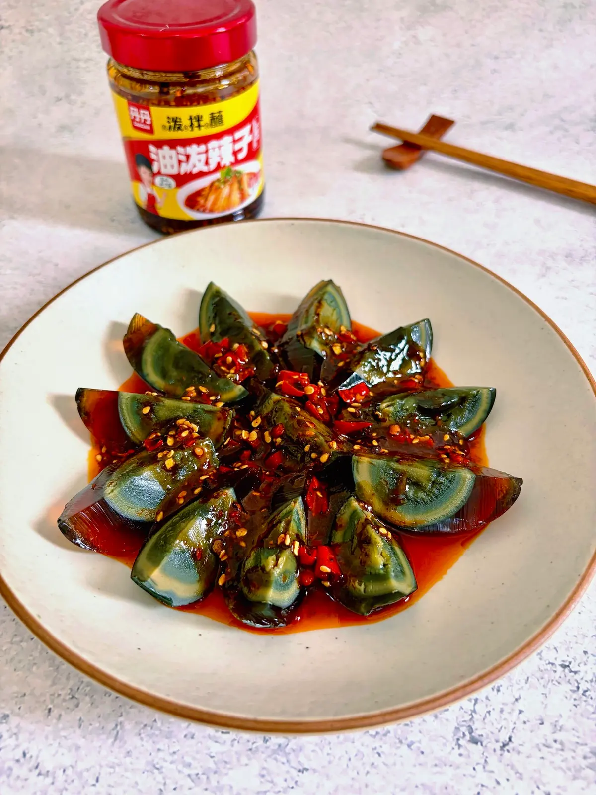 Wedges of dark century egg arranged on a plate under a glossy red chili-soy dressing