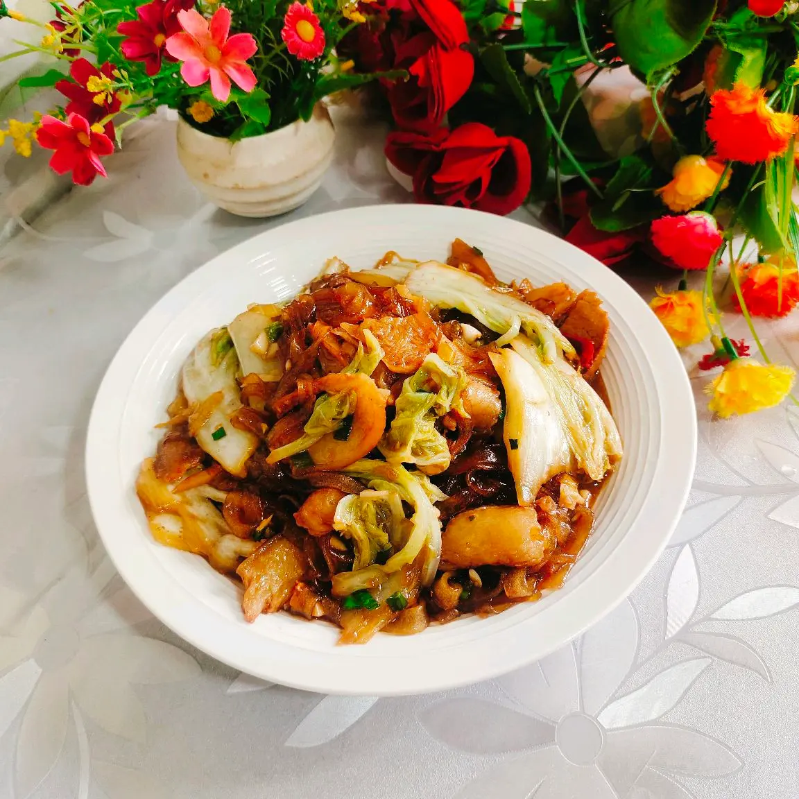A white bowl of cabbage, pork belly slices and translucent glass noodles glazed in dark sauce