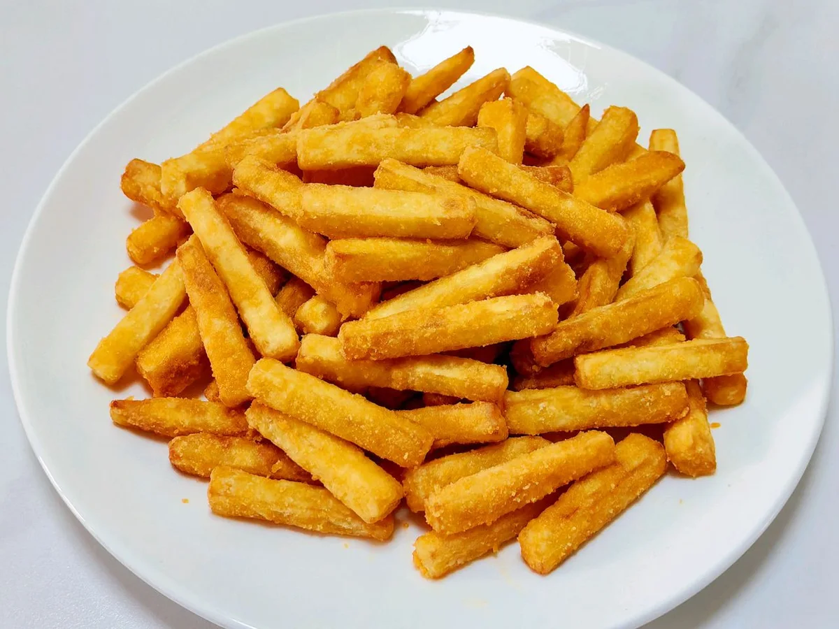 A white plate piled with golden fried sweet potato strips with a crisp starch coating