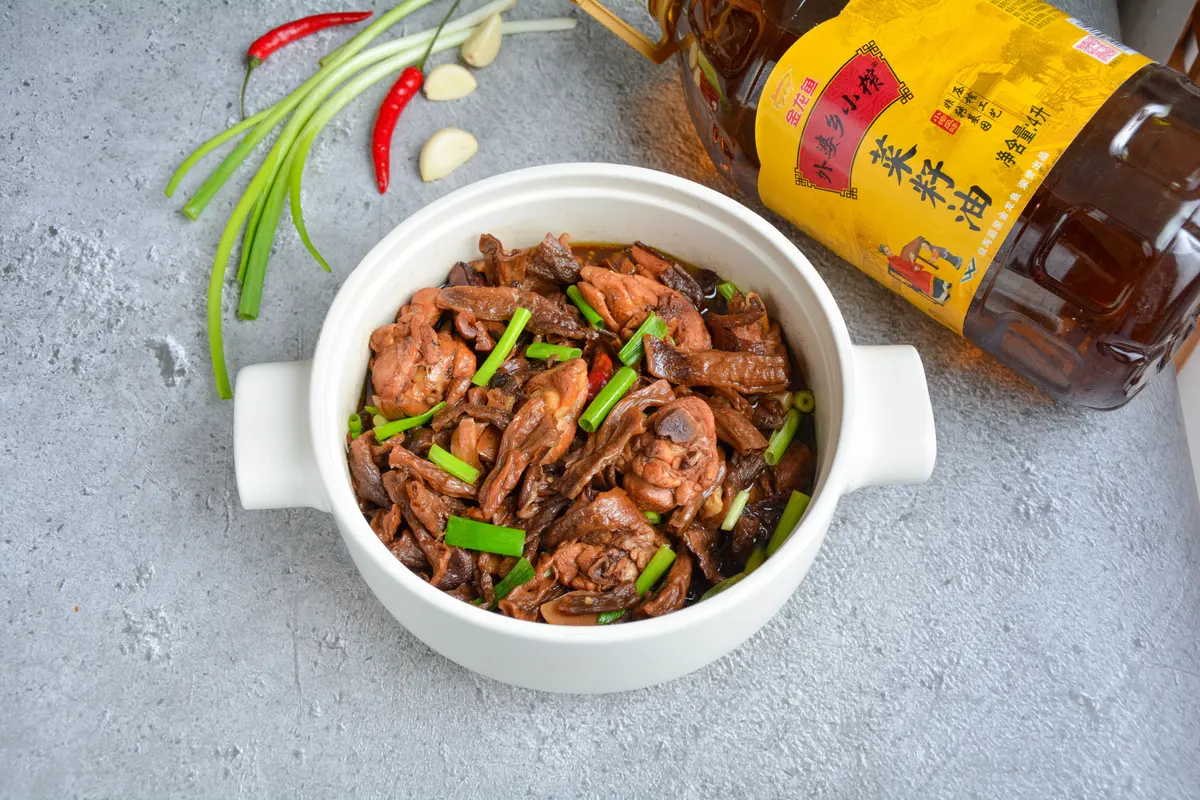 A white ceramic pot of braised chicken legs with dark dried mushrooms and sliced scallion