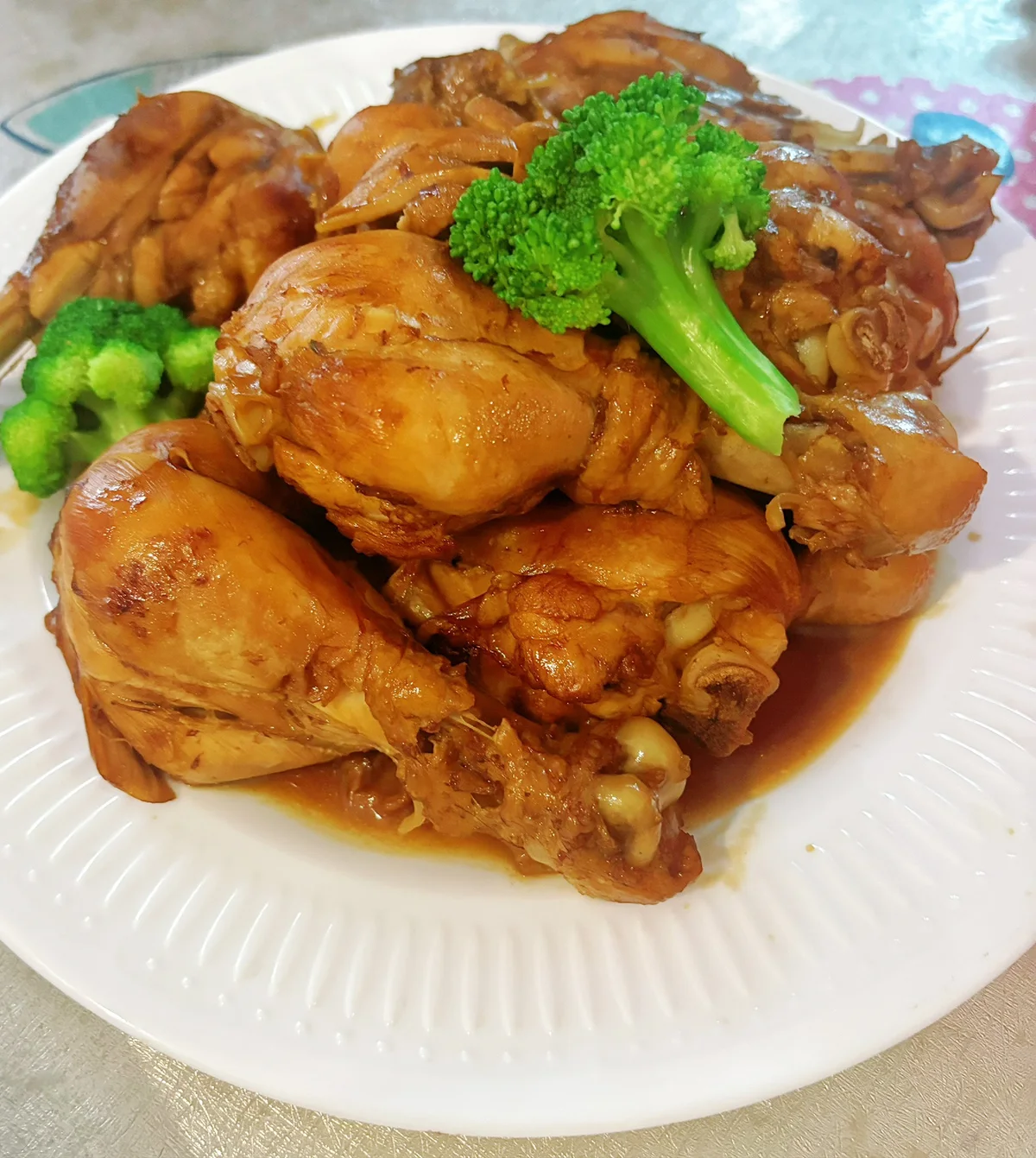 Glossy soy braised chicken drumsticks piled on a white plate with broccoli florets