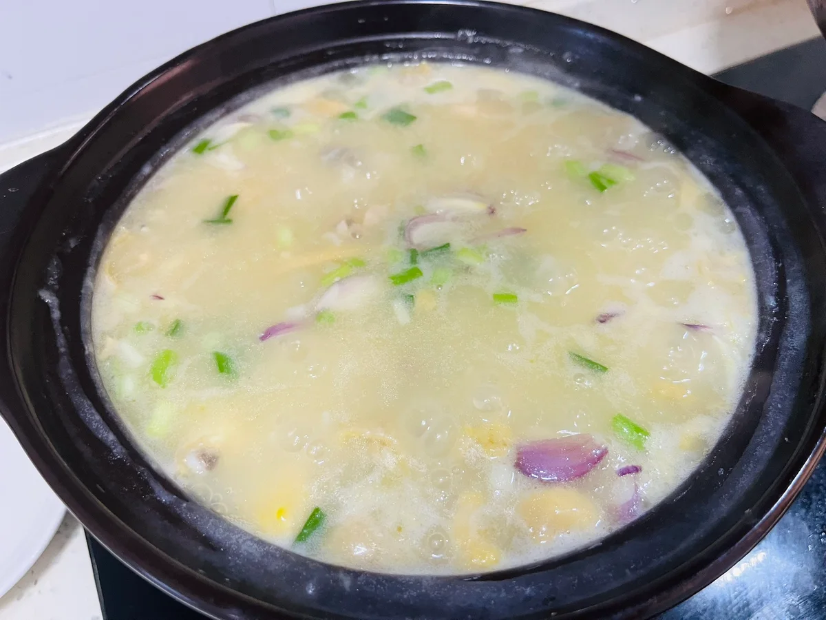A black clay pot of pale chicken congee scattered with chopped spring onion